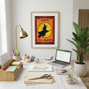 Printable Halloween wall art featuring a folk-art witch silhouette flying past a patchwork moon framed on an office wall