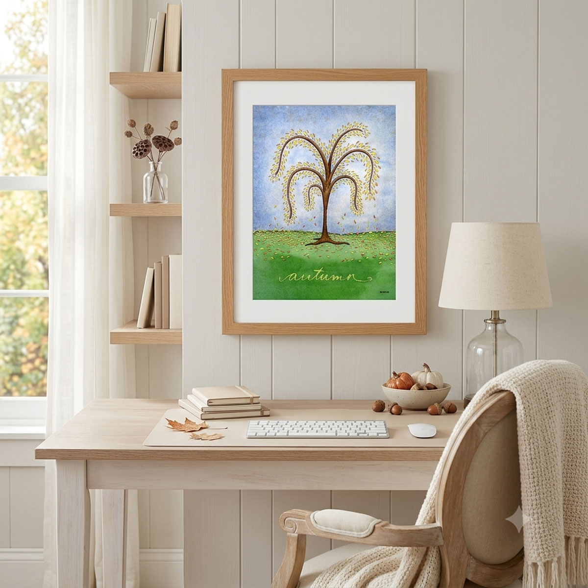 Printable autumn tree wall art featuring a watercolor tree with yellow and orange fall leaves dropping onto a green hill framed on an office wall