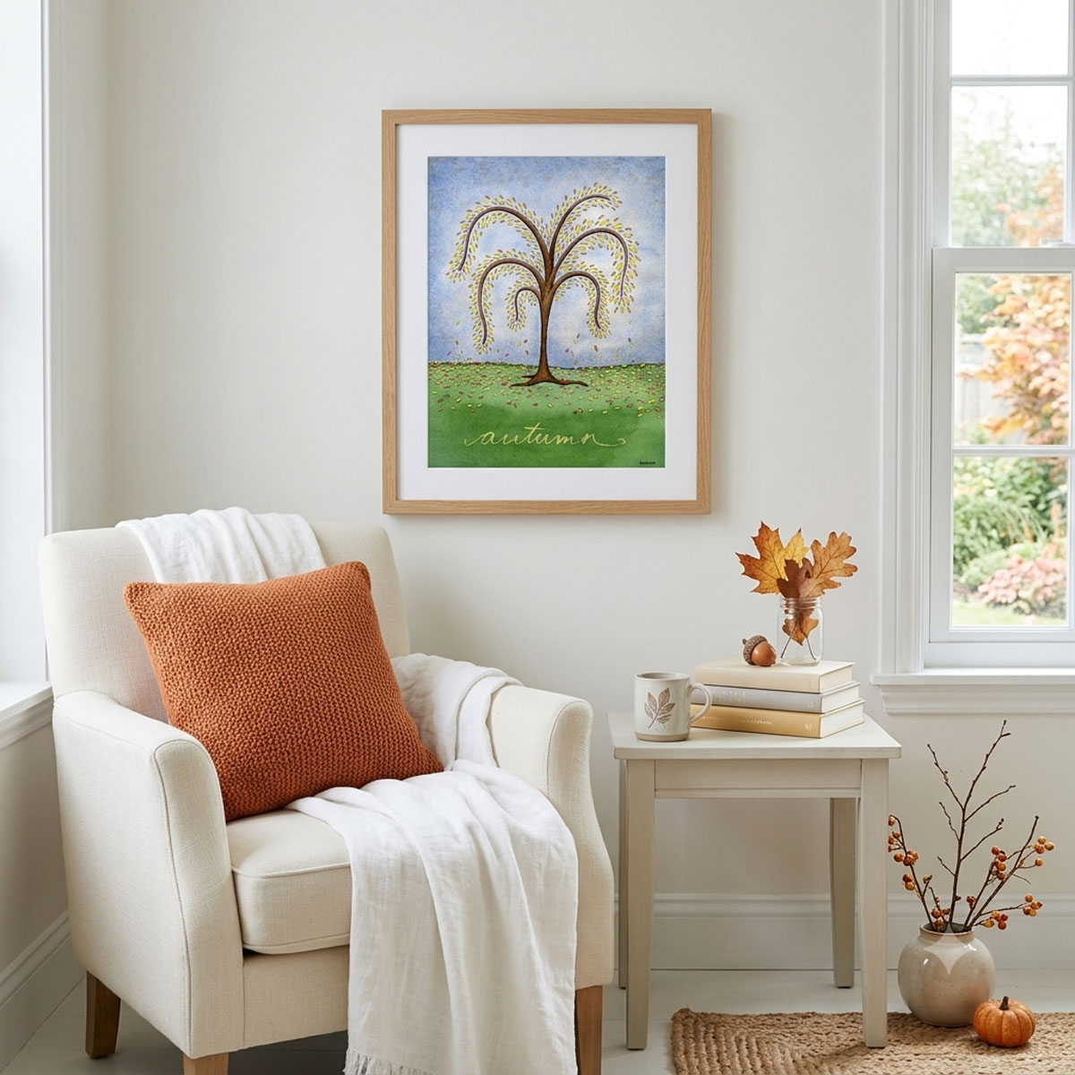 Printable autumn tree wall art featuring a watercolor tree with yellow and orange fall leaves dropping onto a green hill framed in a reading nook