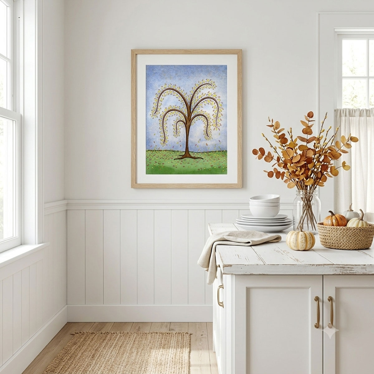 Printable autumn tree wall art with featuring a watercolor tree with yellow and orange fall leaves dropping onto a green hill framed on a kitchen wall