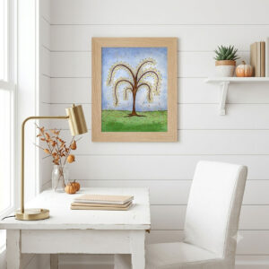 Printable autumn tree wall art with featuring a watercolor tree with yellow and orange fall leaves dropping onto a green hill framed on an office wall
