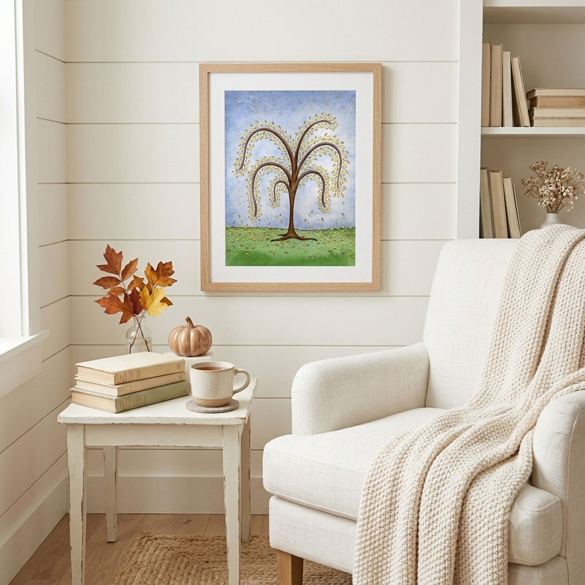 Printable autumn tree wall art with featuring a watercolor tree with yellow and orange fall leaves dropping onto a green hill framed on a reading nook wall