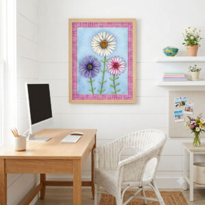 A mock-up photo of a room showing a framed print of a Trio of Daisies Floral Wall Art featuring white, purple, and pink flowers on a blue background with a pink gingham border.
